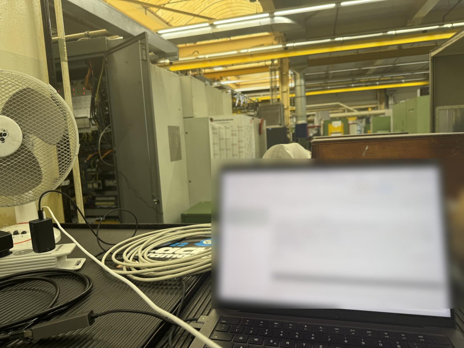 Laptop mit laufendem KI-Agenten auf einem Arbeitstisch in einer Maschinenhalle